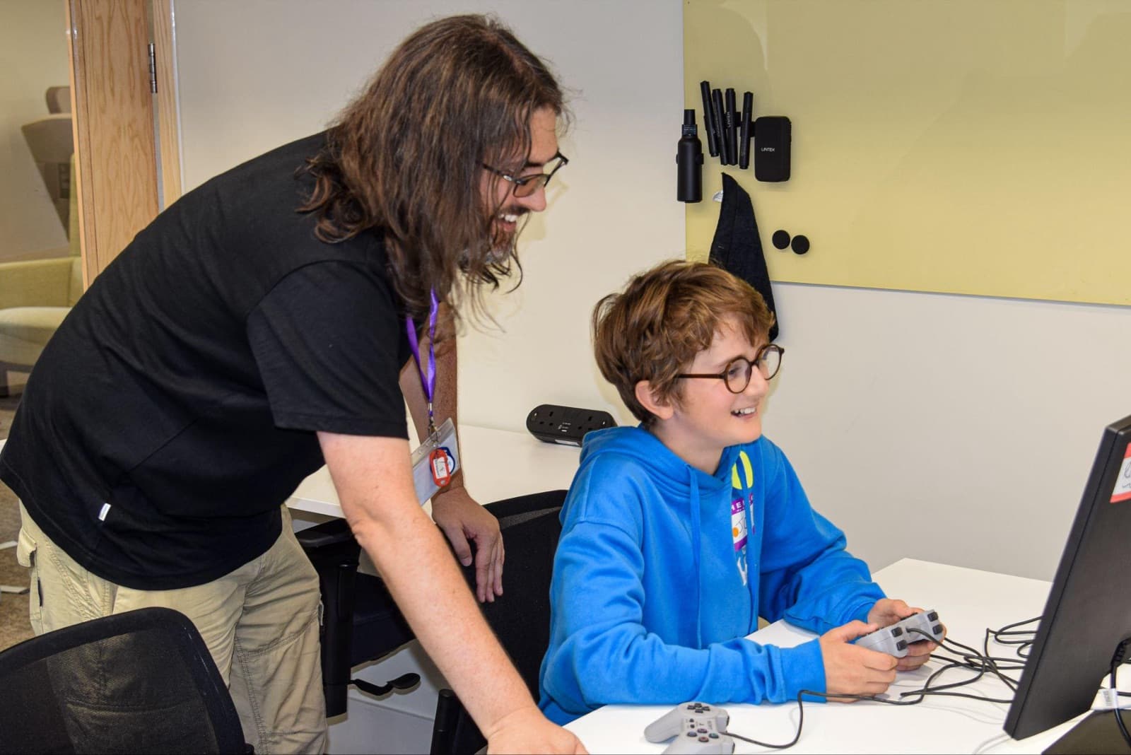 A TechFirst youth mentor and a student laughing together at a retro gaming workshop, games controller in hand