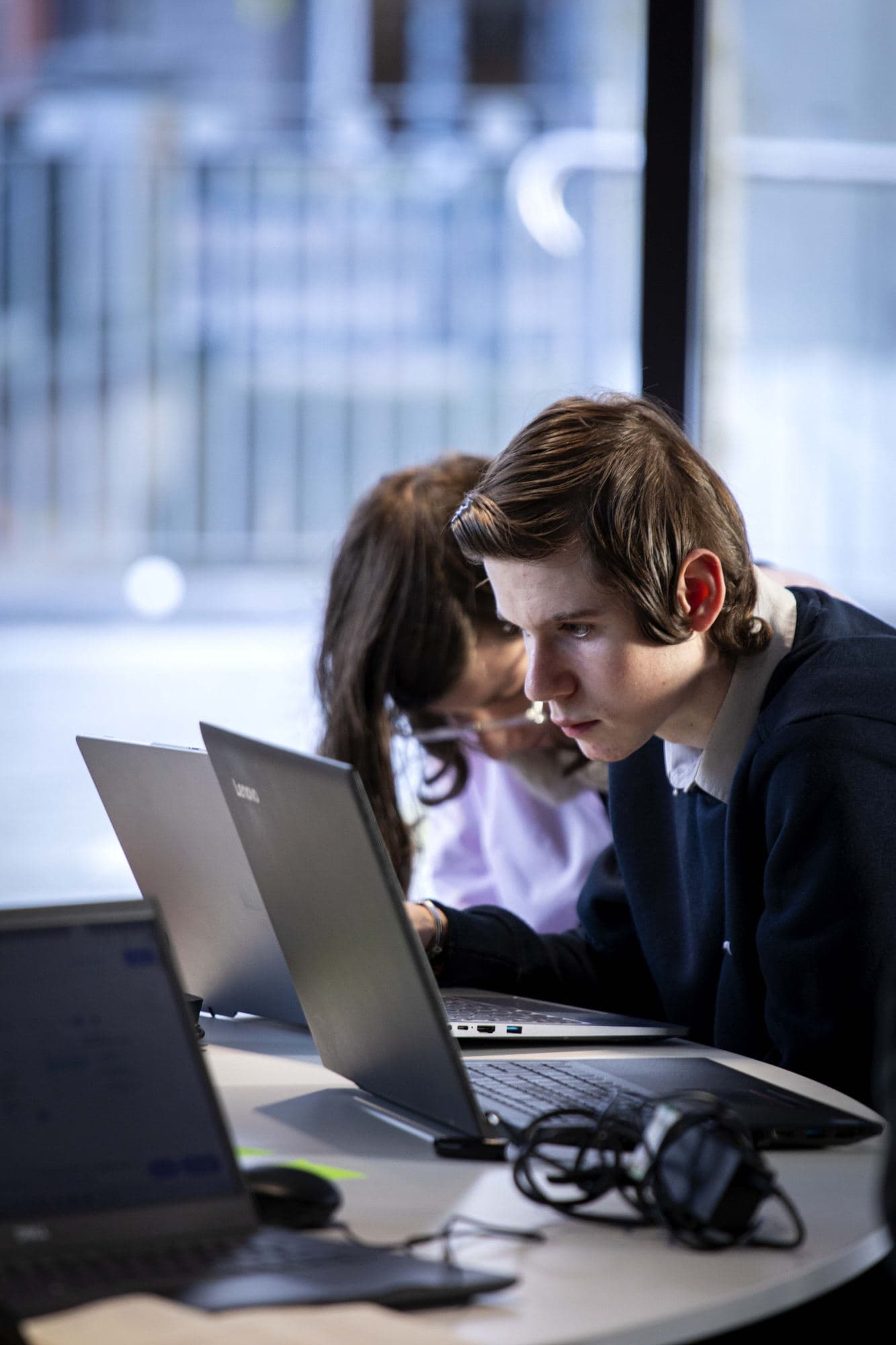 Two students working closely together over a laptop at HackEd